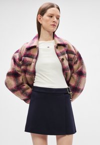 Μπεζ, ροζ και μπορντό τόνοι σε καρό σακάκι από μαλλί, με μεγάλα κουμπιά και χαλαρή εφαρμογή, συνδυασμένο με άσπρη μπλούζα και μαύρη φούστα.