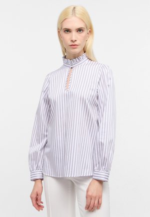 Blusa a righe bianco e lilla con colletto alto, design a chiave di violino e maniche lunghe a sbuffo con dettagli ai polsini. Tessuto dalla consistenza liscia.