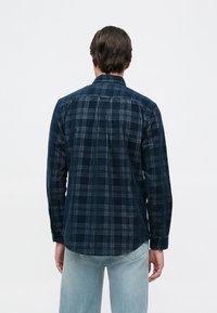 Camisa de franela de cuadros azul marino con mangas largas, puños de botón y dobladillo recto. Textura suave con un patrón de cuadros en un contraste de azul claro.