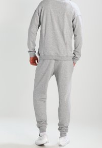 Set di felpa grigia e pantaloni della tuta, caratterizzato da una vestibilità rilassata, polsini a costine e una texture morbida. Include dettagli di cucitura visibili.
