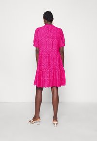 Roze jurk met een gestructureerd oogjesontwerp, korte mouwen, een gelaagde rok en een gegolfde zoom. Gemaakt met lichtgekleurde haksandalen.