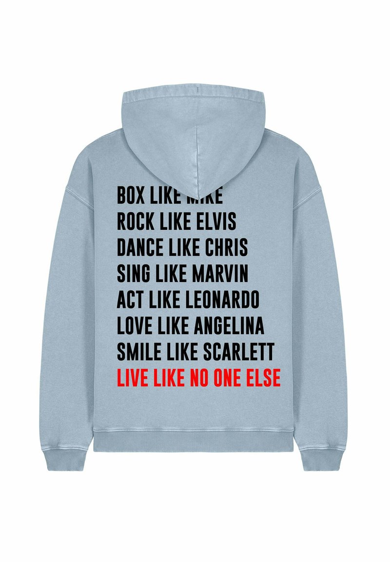 Heled sinine kapuutsiga pusa, mille seljal on musta ja punase tekstiga fraasid ja nimed. Materjal tundub pehme; disain sisaldab nöörist kapuutsi.