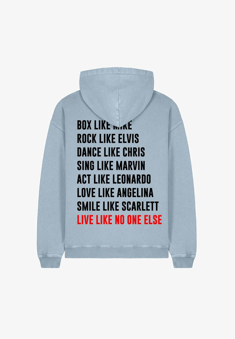 Heled sinine kapuutsiga pusa, mille seljal on musta ja punase tekstiga fraasid ja nimed. Materjal tundub pehme; disain sisaldab nöörist kapuutsi.