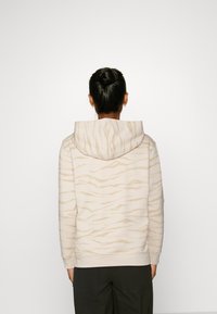 Sweat à capuche beige clair avec un motif rayé tigre texturé. Présente une coupe décontractée et un tissu doux.