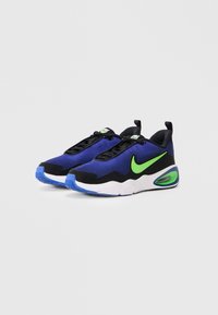 Par u plavih i crnih tenisica s zelenim Nike swoosh-om, bijelim i plavim đonom, i vidljivim zračnim jastučićima na jednostavnoj svijetloj pozadini.