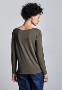 Camicetta verde oliva a maniche lunghe con scollatura ampia, tessuto morbido e vestibilità comoda, abbinata a jeans in denim blu.