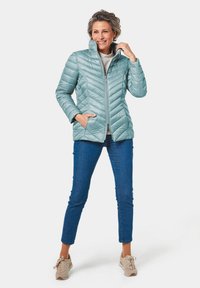 Giacca trapuntata blu chiaro con colletto alto, chiusura con zip e tasche laterali. Abbinata a jeans blu e sneakers beige.