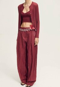 Roter gestrickter Crop-Top, kombiniert mit einer passenden Strickjacke und weit geschnittenen Hosen. Merkmale einen dekorativen Gürtel mit Blumendetails und Metallringen.