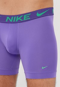 Lilla strækstof boksershorts med en bred, stribet grøn og lilla Nike-logo waistband og en lille grøn Nike swoosh på benet.