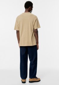 Tricou bej și maro cu dungi, croială lejeră; combinat cu pantaloni albaștri închisi și încălțăminte crem cu șireturi albastre și tălpi negre.