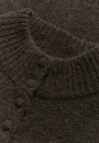 Közelkép sötétbarna gyapjú pulóverről, bordás gallérral és szövetbe burkolt gombokkal a vállvarrás mentén.