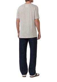 Helles graues T-Shirt mit kurzen Ärmeln und lockerer Passform, aus strukturiertem Stoff, kombiniert mit dunkelblauen weit geschnittenen Jeans und lässigen Schuhen.