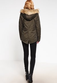 Oliwkowo-zielona parka z kapturem wykończonym sztucznym futrem. Posiada taliowany krój, rozcięcie z tyłu oraz dół wydłużony nieco bardziej z tyłu.