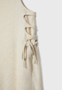 Top beige senza maniche in tessuto di lino testurizzato, con dettagli in pizzo sulle spalle con fettucce annodate e sezioni aperte.