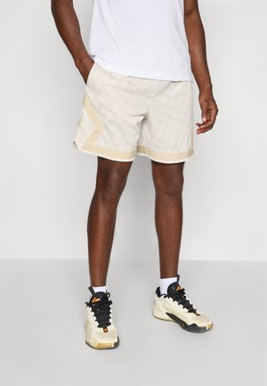 Helle beige Sportshorts mit kleinen Perforationen, gelben Akzenten und einem kontrastierenden Saum. Kombiniert mit schwarzen und beigen Sneakers.