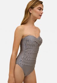 Bañador sin tirantes de una sola pieza en color azul marino con pequeño estampado floral. Presenta detalles de fruncido y un diseño ajustado, resaltando una textura suave.