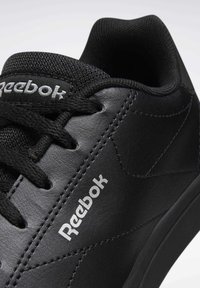 Black athletic shoe with smooth synthetic leather material, textured mesh tongue, laces, and silver logo detail on the side.