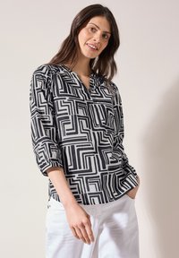 Blusa de patrón en blanco y negro con escote en V, mangas de tres cuartos y un corte holgado; la tela parece ligera y suave.