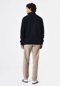Marineblauwe gebreide trui met hoge kraag, met ribbeltextuur en omgeslagen mouwen, gecombineerd met lichtbeige corduroy broek en gestreepte schoenen.