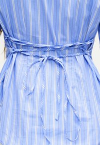 Πλάτη μπλε και λευκού κάθετα ριγέ φόρεμα με δύο δεμένες ζώνες στη μέση που σχηματίζουν φιόγκο στο κέντρο.