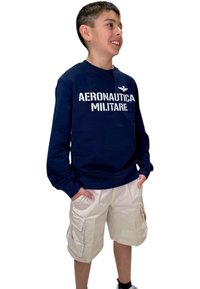 Felpa blu navy con testo bianco "AERONAUTICA MILITARE". Abbinata a pantaloni cargo beige chiaro dotati di tasche laterali.