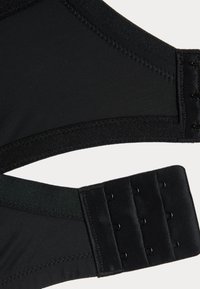 Gros plan sur la sangle arrière d'un soutien-gorge noir avec trois rangées de crochets et œillets, et des coutures détaillées sur les panneaux en tissu.