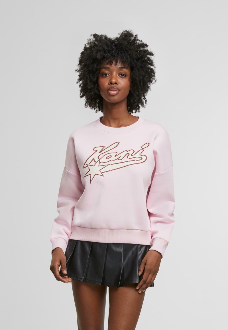 Felpa rosa con logo "Kani" e design a stelle, realizzata in tessuto morbido, dotata di scollatura rotonda e vestibilità rilassata, abbinata a una gonna nera plissettata.