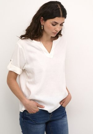 Camicia bianca di lino con scollatura a V e maniche arrotolate, caratterizzata da una sottile texture e una vestibilità comoda. Abbinata a jeans in denim blu.