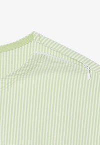 Tissu de chemise rayé vert et blanc avec une texture lisse. Doté d'une ouverture zippée au niveau de l'encolure. Marque visible sur le col.