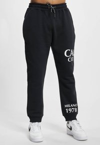 Schwarze Sweatpants aus einem weichen Stoff, mit einem Kordelzugbund, weißem Drucktext am linken Bein und Bündchen an den Säumen.