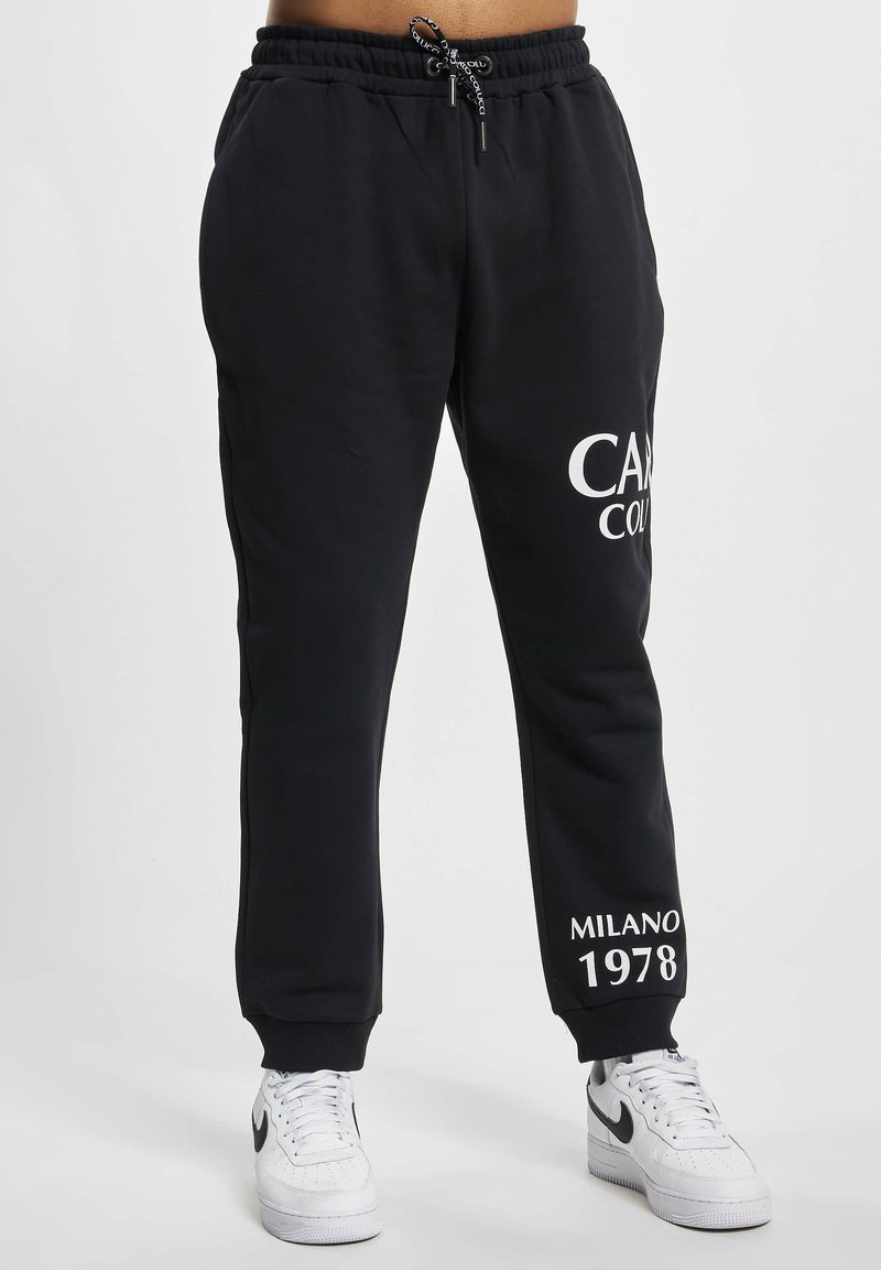 Schwarze Sweatpants aus einem weichen Stoff, mit einem Kordelzugbund, weißem Drucktext am linken Bein und Bündchen an den Säumen.