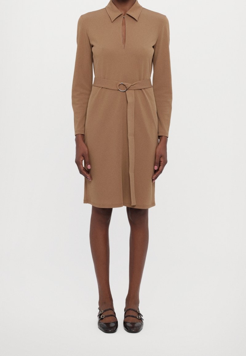 Robe marron à manches longues avec un col, un décolleté en forme de goutte, une ceinture à la taille ornée d'un anneau métallique, et une coupe droite tombant au-dessus du genou.