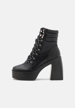 Bottine plateforme en cuir noir avec col matelassé, laçage devant avec œillets métalliques, talon bloc et semelle épaisse.