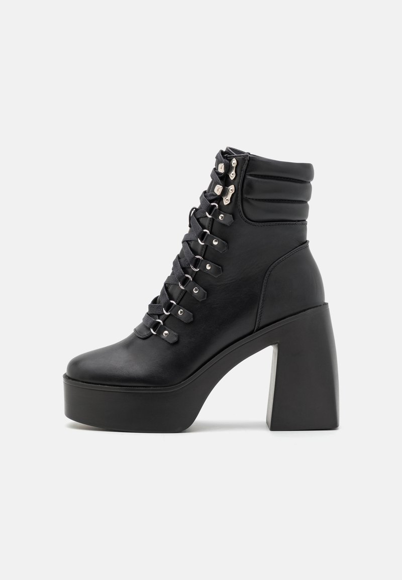 Bottine plateforme en cuir noir avec col matelassé, laçage devant avec œillets métalliques, talon bloc et semelle épaisse.