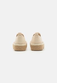 Espadrillas in tela beige con suola in juta, caratterizzate da una forma arrotondata e un anello posteriore per facilitare l'indossamento. Texture liscia, design minimale.