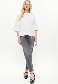 Maglione grigio con una forma ampia e maniche larghe lunghe fino al gomito, abbinato a jeans grigi e scarpe nere con tacco alto e cinturini alla caviglia.