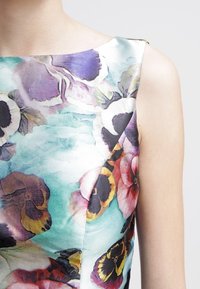 Vestido sin mangas con estampado floral que presenta una tela texturizada en colores vibrantes, incluidos acentos en púrpura, rosa, amarillo y azul.