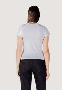 Witte t-shirt met korte mouwen en een ronde halslijn, met een gladde textuur en een slim fit ontwerp, gecombineerd met zwarte jeans met achterzakken.