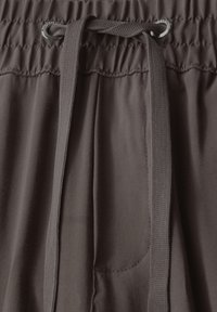 Mörkbruna byxor med elastisk midja och dragsko samt en liten sidoficka, tillverkade av ett slätt tyg med en subtil lyster och draperad midja.