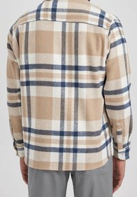 Beżowa flanelowa koszula w kratę z granatowymi, kremowymi i brązowymi kwadratami. Posiada kołnierz i mankiety zapinane na guziki. Teksturowany, miękki materiał.