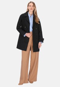 Palton negru cu nasturi dubli și guler larg, însoțit de o cămașă albastru deschis și pantaloni largi bej. Textură fină și croială ajustată.