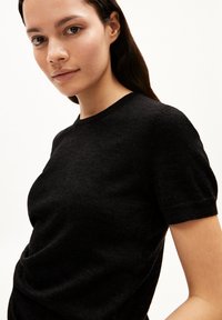 Zwart kortemouwen trui van een zacht, structuurstof met een ronde halslijn en een aansluitende pasvorm, voorzien van subtiele ribbelaccenten op de mouwen.