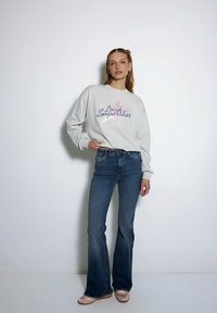 Jasnoszara bluza z grafiką "Local Superstar", w połączeniu z niebieskimi dzwonami i cielistymi balerinami. Gładki materiał i luźny krój.