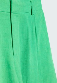 Gonna plissettata verde con tessuto testurizzato, caratterizzata da una vita piatta e cuciture verticali, che mostra una finitura vivace e liscia.