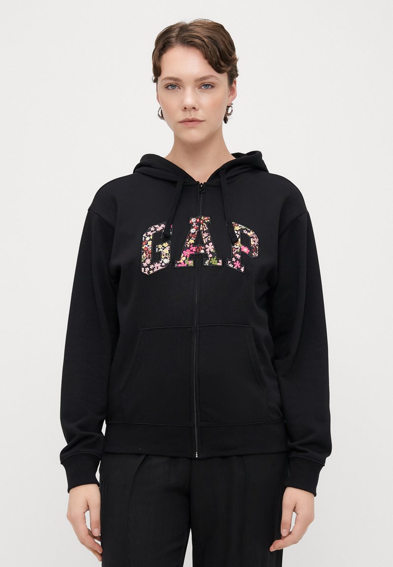 Črni zip-up dukserica z rožnatim logotipom "GAP", z kapuco na vrvico in sprednjimi žepi. Gladek material, sproščen kroj in rebrasti manšeti.