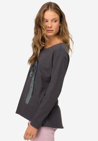 Camisa de manga larga gris oscuro con un escote redondeado y un diseño gráfico en azul claro que presenta un animal. Material de algodón suave, ajuste relajado.