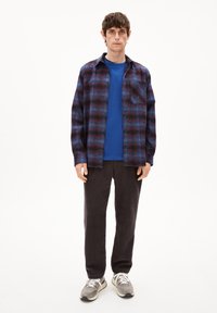 Herenoutfit met een geruite flanellen overhemd in donkerblauw en rood, een blauwe t-shirt en donkere corduroy broek, gecombineerd met grijze en witte sneakers.