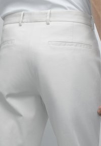 Witte katoenen broek met een gladde textuur, een getailleerde pasvorm, riemlussen en twee achterzakken met een subtiele naaddetail.