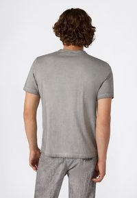 Szara koszulka z krótkim rękawem, z okrągłym dekoltem, wykonana z miękkiego materiału, z delikatną fakturą i detalem logo na dolnym brzegu.