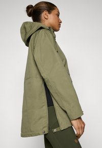 Olijfgroen parka met een capuchon, voorzien van zijritsen, knoopdetails en een relaxte pasvorm. Glad, duurzaam materiaal met een matte afwerking.